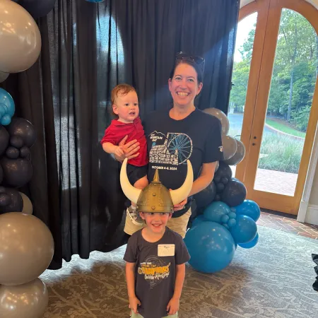 a person holding a baby and standing next to a boy with balloons