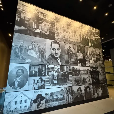 Large black and white photo collage displayed on a wall featuring historical images and portraits in a dimly lit room.