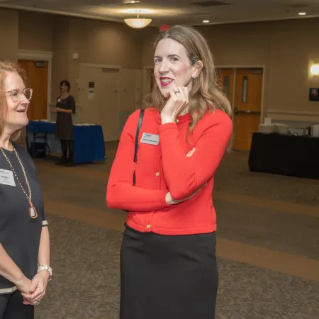 Two women in business attire chatting casually in a carpeted conference room with name tags.