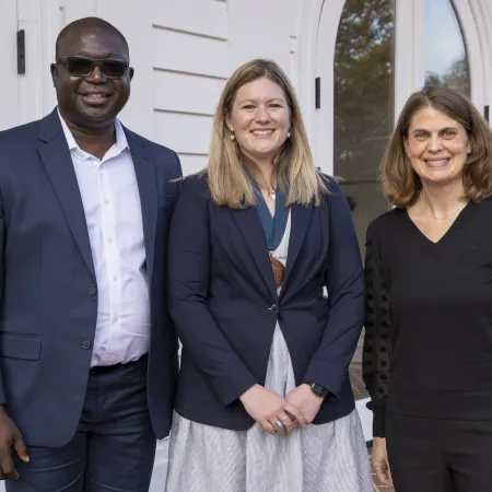 Three professionals smiling and standing outdoors in business casual attire in front of a white building.