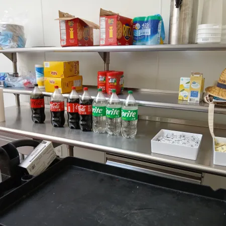 Stainless steel kitchen shelves with soda bottles, snack boxes, paper towels, and a straw hat on the side.