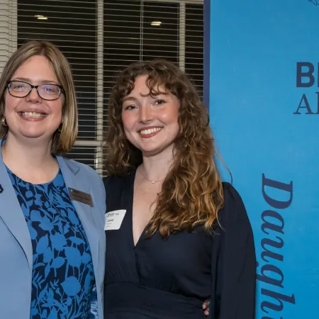 Two smiling women posing at a professional event with blue-themed attire and a branded backdrop.