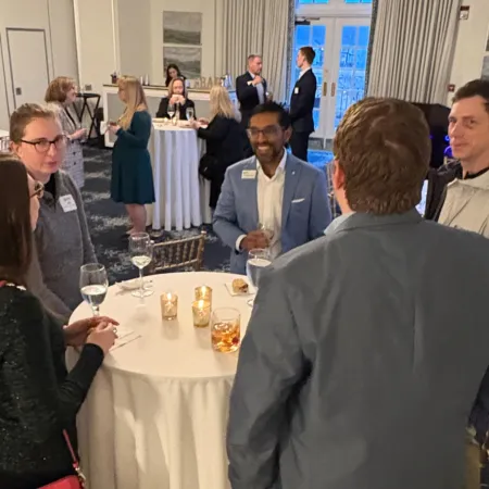 Group of business professionals networking and conversing at a formal indoor event with drinks and name tags.