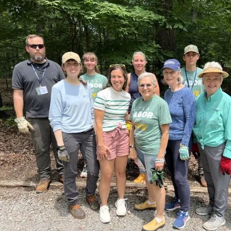 Group of diverse volunteers wearing gloves and casual clothes posing outdoors in a wooded area on a sunny day