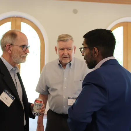Three men in business attire engaged in conversation at a networking event indoors with arched windows.