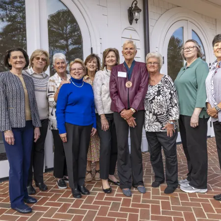 Group of ten older women standing outside a building with white doors and brick walkway, smiling and posing for photo.