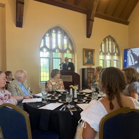 Speaker addressing an audience in a historic room with arched windows during a formal event.