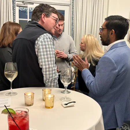 Group of people engaged in conversation around a table with drinks and candles in an indoor setting.