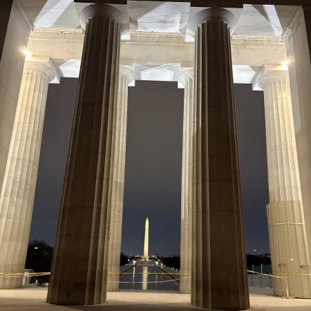 Night view of the Washington Monument framed by illuminated columns of the Lincoln Memorial in Washington DC.