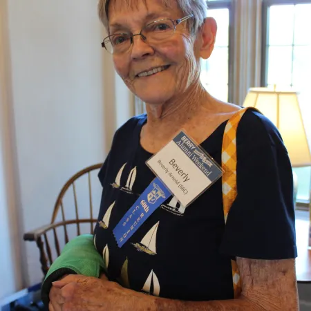 Elderly woman with a green arm cast smiling indoors wearing a navy blue shirt and name badge.