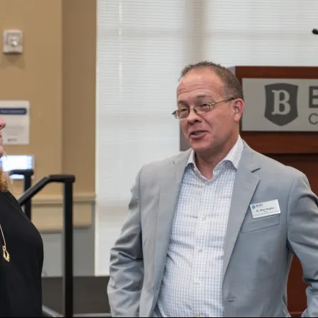 Two professionals engaged in conversation at a conference or seminar in a formal setting.