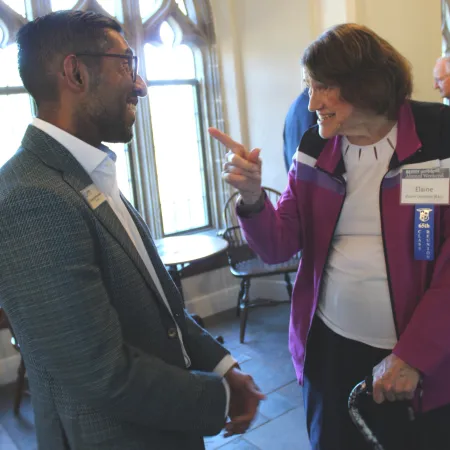 Elderly woman with cane engaging in conversation with man in suit inside bright room with arched windows