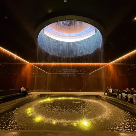 Indoor water feature with circular skylight above and illuminated waterfall surrounded by seated visitors
