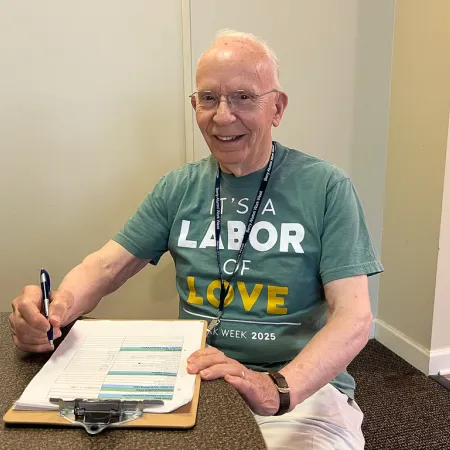 Elderly man smiling and filling out a form on a clipboard at a table in a casual indoor setting.