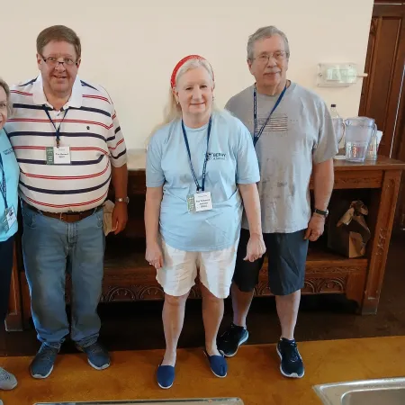 Four adults standing indoors in casual clothing with name badges and lanyards, smiling at the camera.