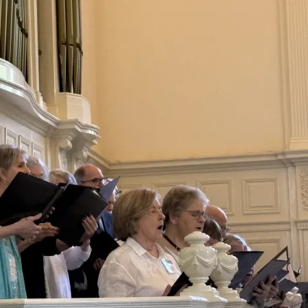 Group of senior choir members singing together inside a bright church with organ pipes in the background