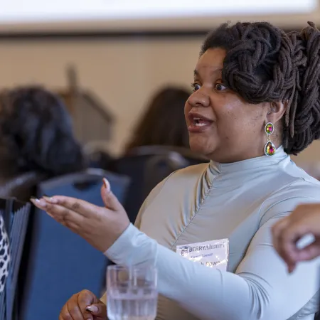 Woman with dreadlocks speaking and gesturing during a conference or meeting in a professional setting.