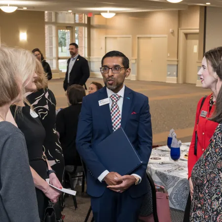 Group of professionals conversing at a formal indoor networking event with tables set for dining.