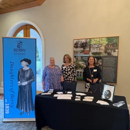 Three women stand behind a table with brochures and a banner reading Daughters of Berry, est. 1939, at Berry Alumni event.