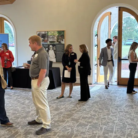Professionals networking and conversing at a business event in a bright room with arched doorways and patterned carpet.
