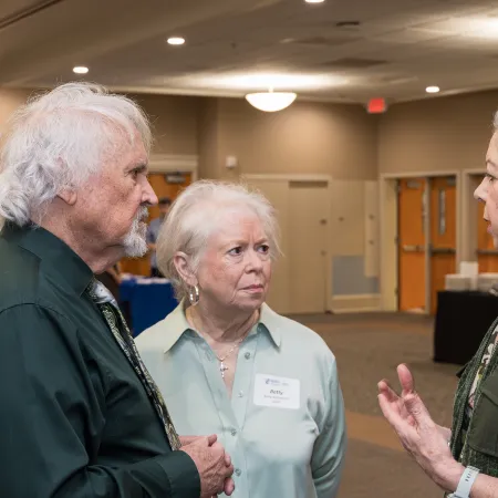 Three adults engaged in serious conversation in a spacious, well-lit indoor meeting room.