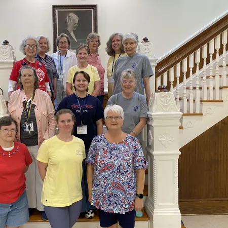 Group of senior women posing on staircase inside a historic building with a framed portrait above them.