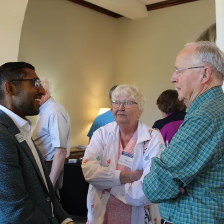 Three people engaged in a friendly conversation at an indoor social event in a well-lit room.
