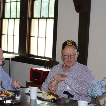 Two elderly men enjoying breakfast together at a wooden table with natural light from large windows.