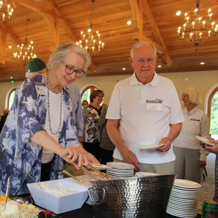Seniors enjoying a buffet in a wooden ceiling dining hall with chandeliers during a social event.