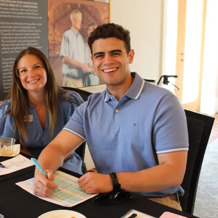 Smiling man and woman seated at table, filling out forms with pens, papers, and snacks on a black tablecloth.