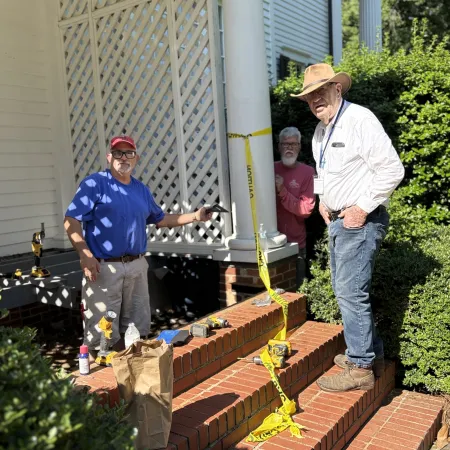 Three men working on brick stairs repair outside a white house with caution tape and tools visible.