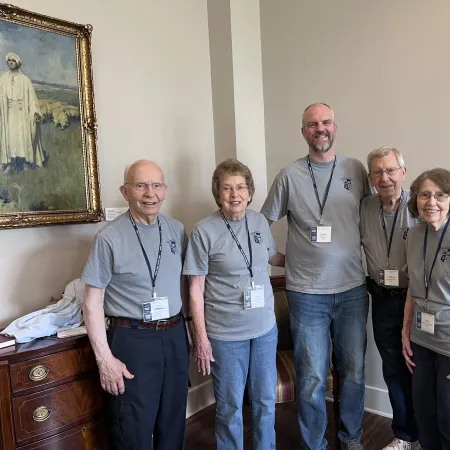 Group of five people wearing matching gray shirts and name tags standing indoors, smiling at the camera.