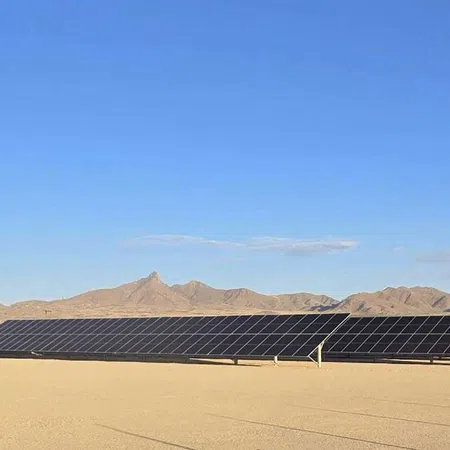 Solar panels installed on a desert landscape with mountains in the background under a clear blue sky.