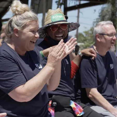Team of diverse adults laughing and clapping at an outdoor event wearing matching shirts with logo
