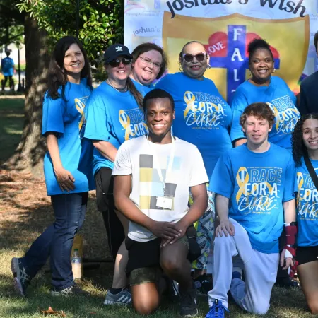 Group of diverse people wearing blue Race for a Cure shirts posing outdoors at a charity event.