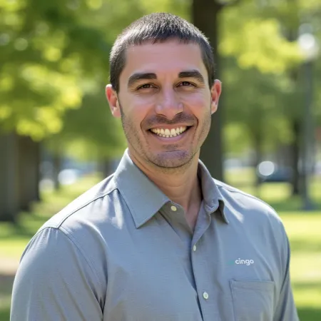 Smiling man wearing a gray Cingo branded shirt standing outdoors with blurred green trees in the background
