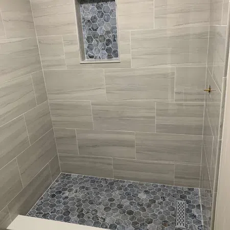 Modern shower with large rectangular wall tiles and dark hexagonal mosaic floor tiles with a drain.