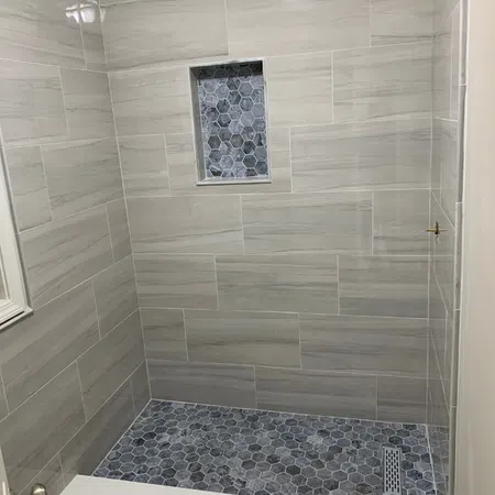 Modern shower stall with gray rectangular wall tiles and blue hexagonal floor and niche tiles.