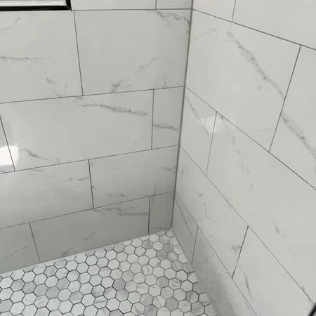 Shower corner with large marble-effect rectangular wall tiles and small hexagonal floor tiles in gray tones.
