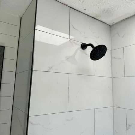 Modern shower with black showerhead and white marble-style tiles on walls in a bathroom corner.