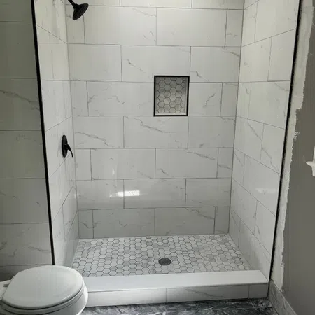 Modern walk-in shower with white marble tiles and hexagon floor tiles next to a white toilet.