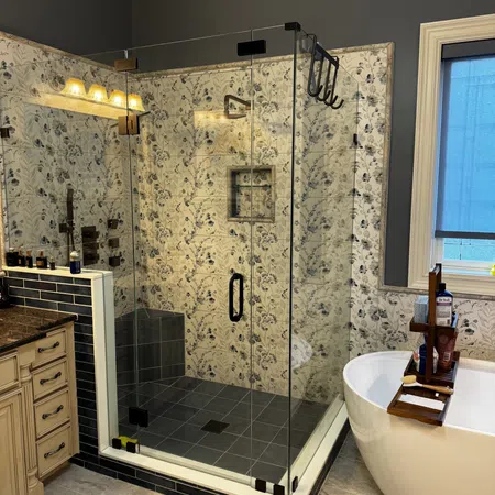 Modern bathroom with glass shower, floral tile walls, freestanding tub with wooden tray, and dark blue accents.
