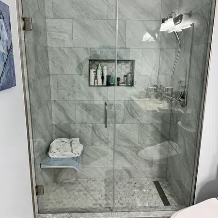 Modern bathroom shower with glass door, marble tiles, built-in shelf, and folded towels on bench.