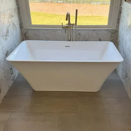 White freestanding bathtub with modern faucet under a large window overlooking a grassy yard.
