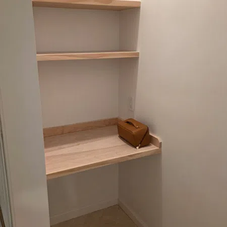 Small corner workspace with two wooden shelves and a wooden desk holding a brown leather bag.