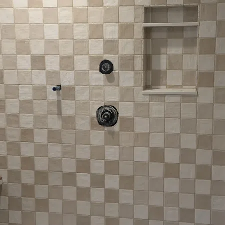 Beige and cream checkered tiled shower wall with built-in niche and exposed plumbing fixtures.