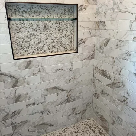 Shower corner with marble subway tiles and pebble mosaic floor and niche with glass shelf.