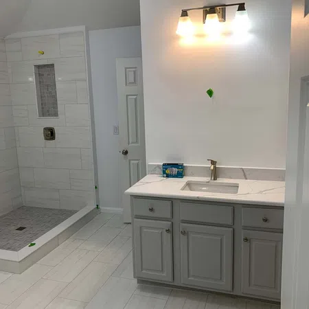 Modern bathroom with gray vanity, white countertop, built-in shower with tiled walls and floor, and overhead lighting.
