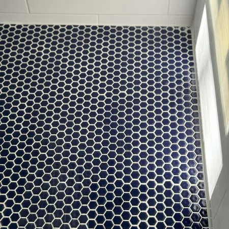 Dark blue hexagonal floor tiles with white grout in a modern bathroom corner with white wall tiles.