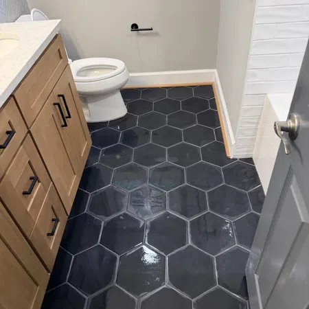 Bathroom floor with large glossy black hexagonal tiles next to a wooden vanity and white toilet.